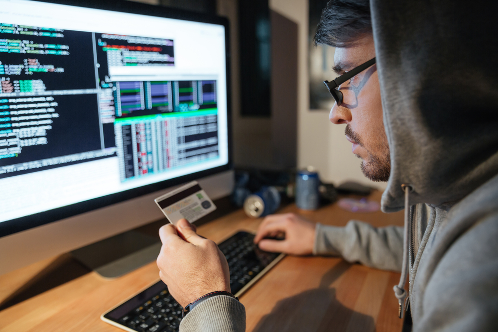 Concentrated young hacker in glasses stealing money from different credit cards sitting in dark room-2